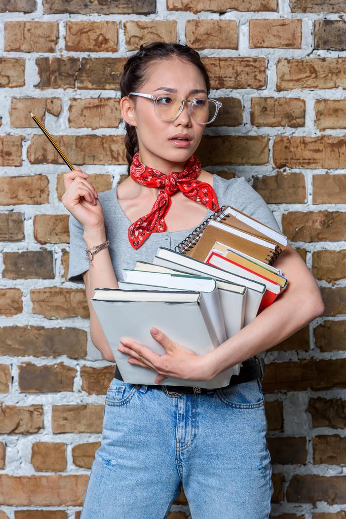 Porträt eines nachdenklichen asiatischen Studenten mit Büchern und Bleistift - Foto, Bild