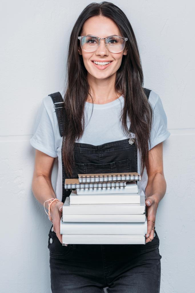 Porträt eines lächelnden kaukasischen Studenten, der Bücher in der Hand hält und in die Kamera blickt - Foto, Bild