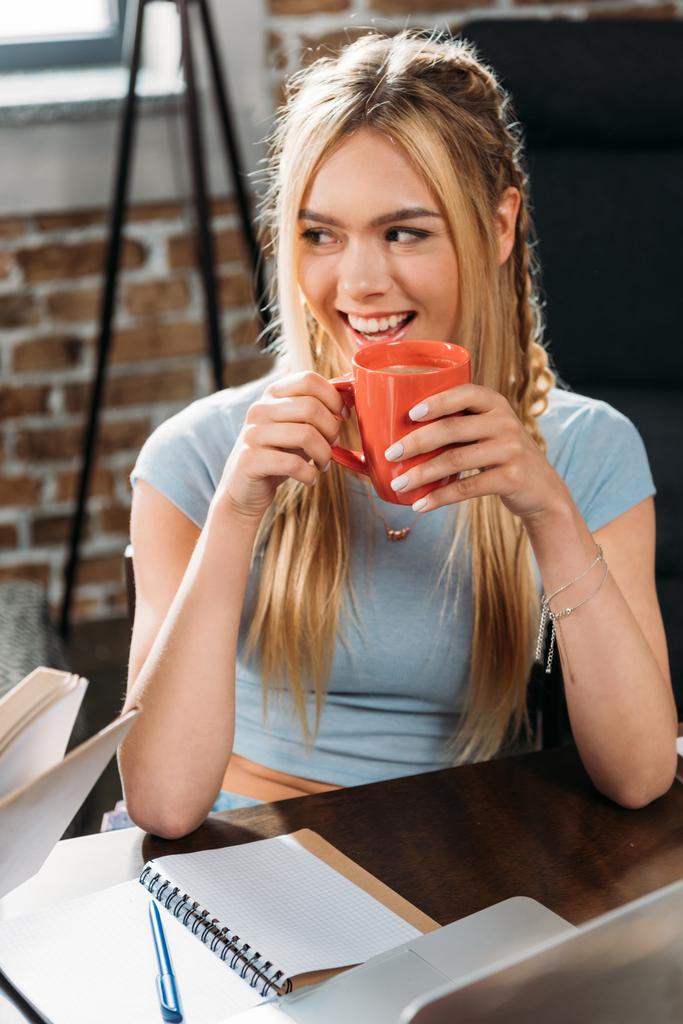 молода усміхнена біла жінка п'є каву, сидячи за столом
 - Фото, зображення
