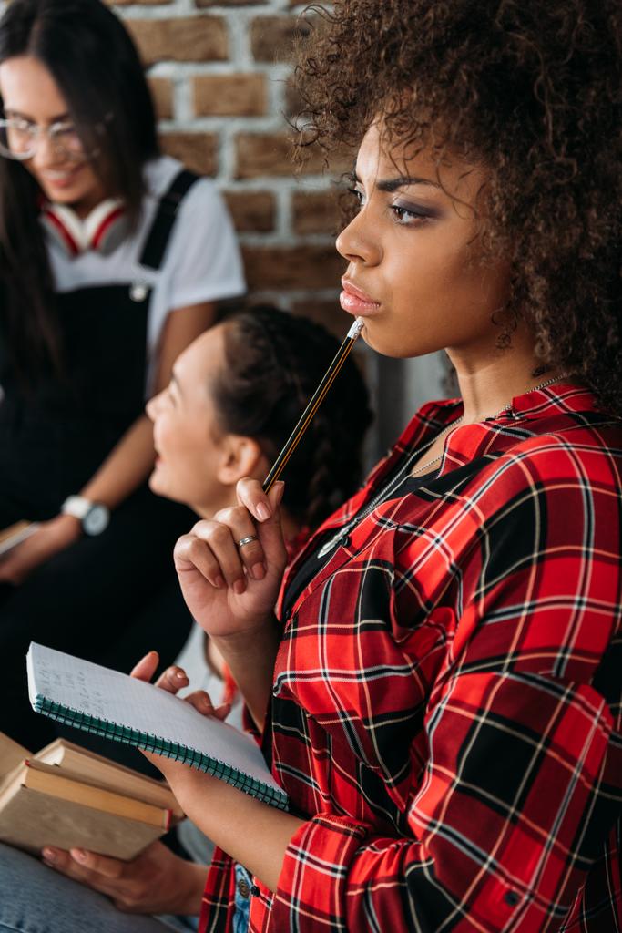 afro-amerikai lány gazdaság notebook átgondolt jelent, miközben beszélt barátai - Fotó, kép