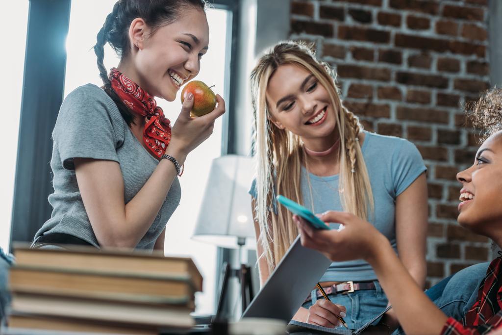 Hymyilevät nuoret naiset, joilla on omena ja älypuhelin, puhuvat ja katsovat toisiaan
 - Valokuva, kuva