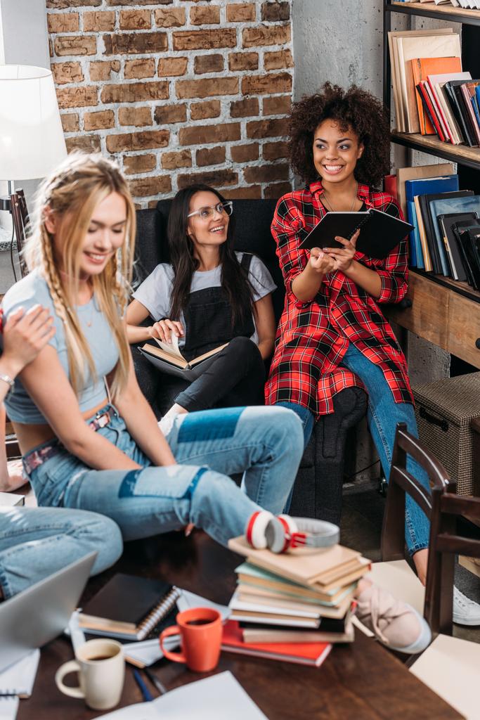 Hymyilevät nuoret naiset istuvat ja opiskelevat yhdessä kirjojen kanssa
 - Valokuva, kuva