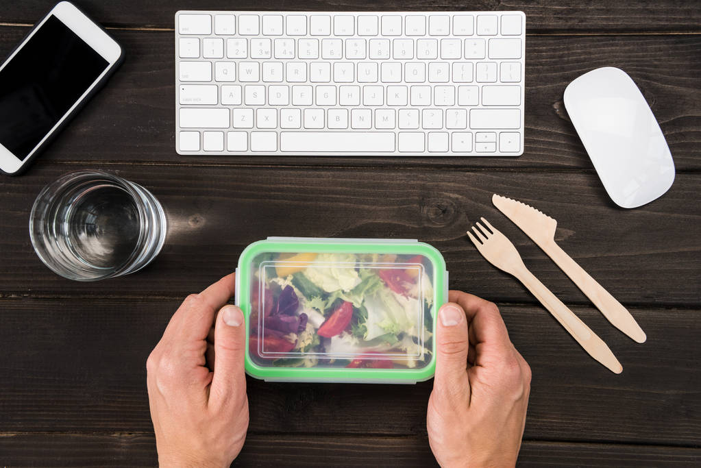 Felülnézet munkahelyi digitális eszközök és emberi kéz képes enni saláta munka során - Fotó, kép