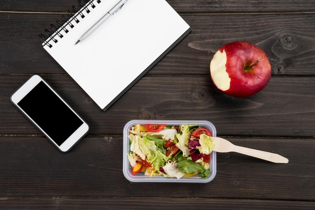Top view of organic salad with apple, notebook and smartphone on wooden table - Photo, Image