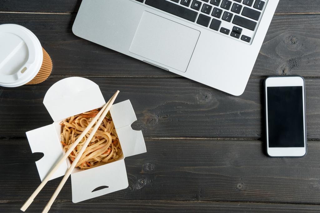 top view of noodle with chopsticks and laptop with coffee to go on wooden tabletop - Photo, Image