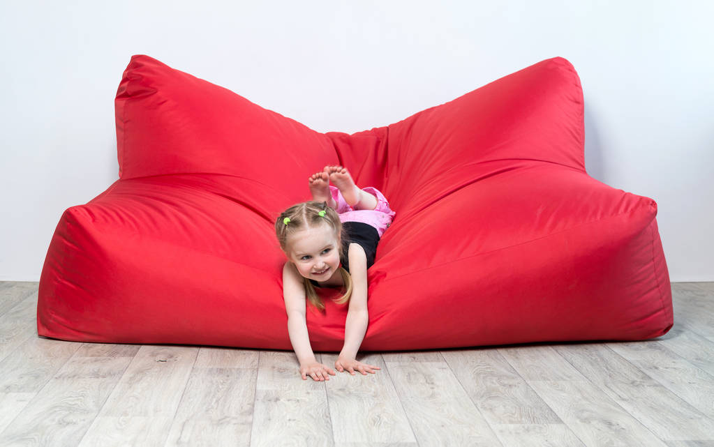 niña preescolar acostada en un gran sofá rojo
 - Foto, imagen