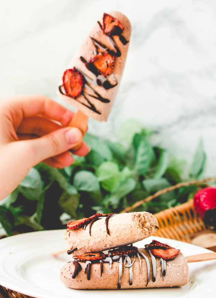 Hand hält ein Eis am Stiel mit Schokolade und Erdbeeren - Foto, Bild