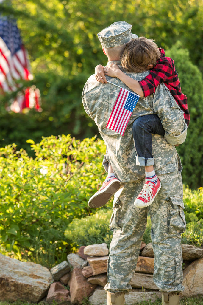Щасливе возз'єднання солдата з сім'єю на відкритому повітрі, батько обіймає сина
 - Фото, зображення