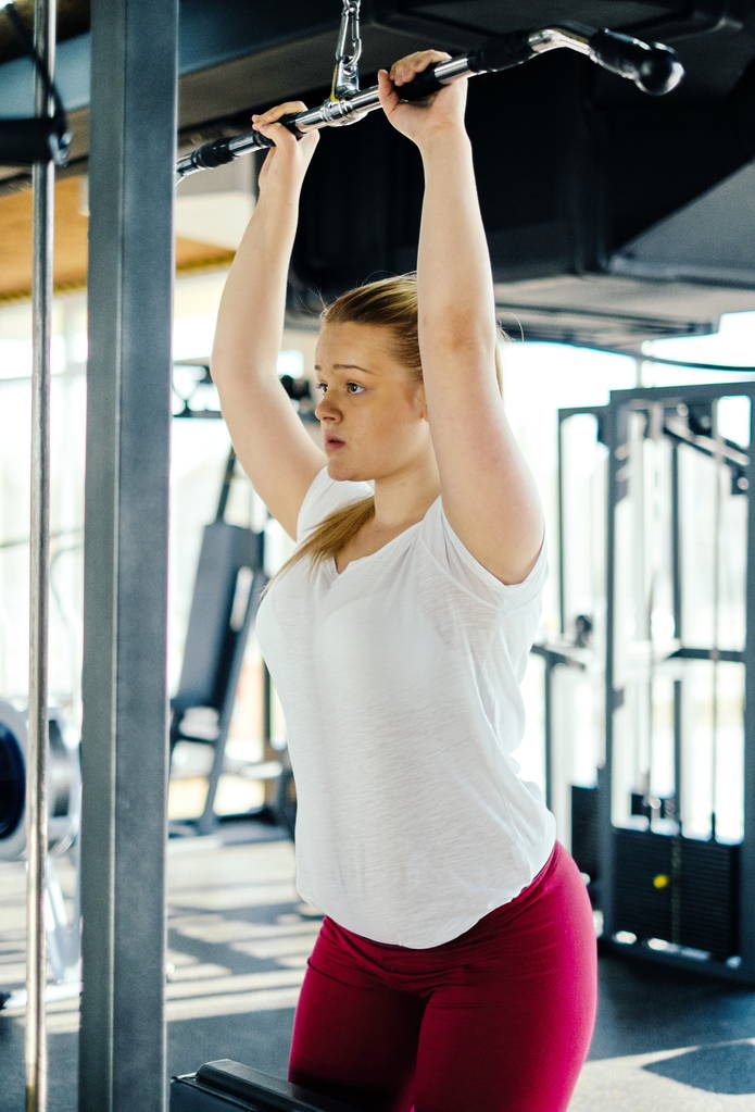 Young beginner girl exercising in the fitness gym, with lat machine - Photo, Image