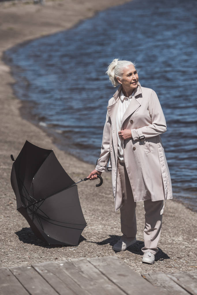 Seniorin posiert mit Regenschirm am Flussufer - Foto, Bild