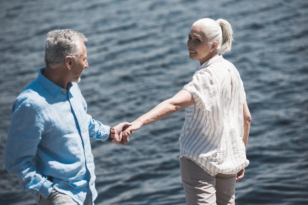 elderly couple holding hands on riverside - Photo, Image