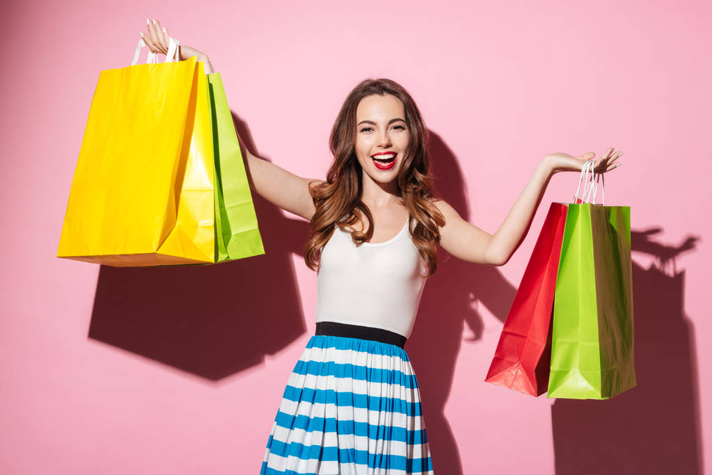 Onnellinen tyttö kuljettaa värikkäitä ostoskasseja eristetty vaaleanpunainen tausta
 - Valokuva, kuva