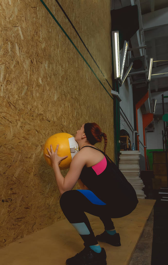 Молода жінка вправляється, кидаючи м'яч в спортзал
 - Фото, зображення