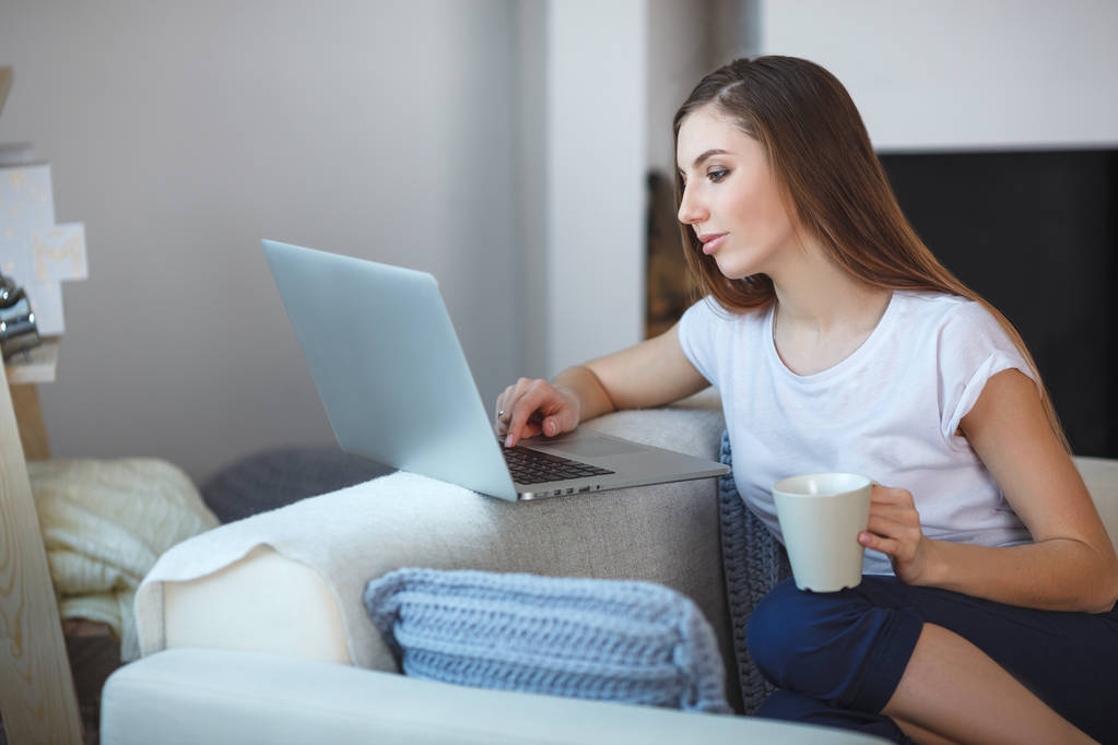 νεαρή γυναίκα που κάθεται με το laptop στον καναπέ στο σπίτι της - Φωτογραφία, εικόνα