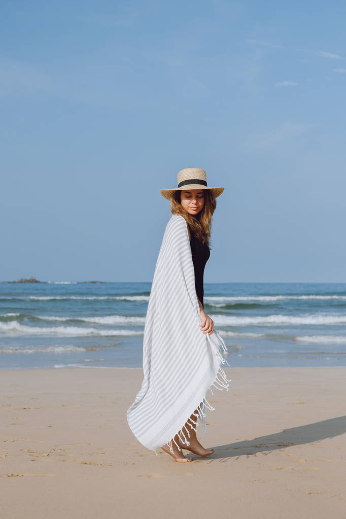 Chica en un traje de baño negro y sombrero caminando por la playa
  - Foto, imagen