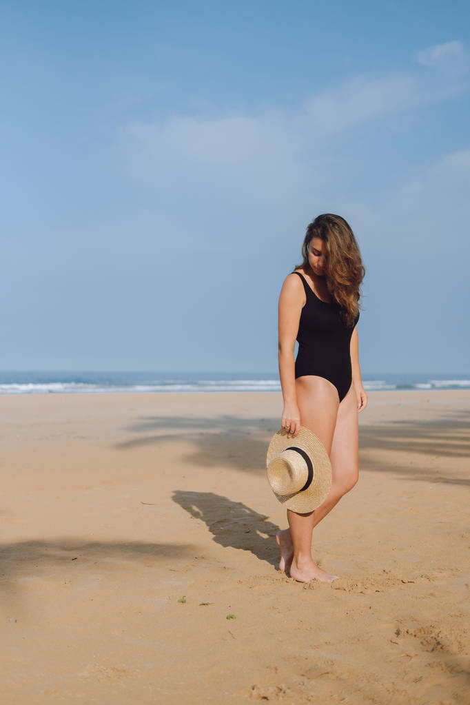 Kız bir siyah mayo ve sahilde yürüyüş şapka - Fotoğraf, Görsel