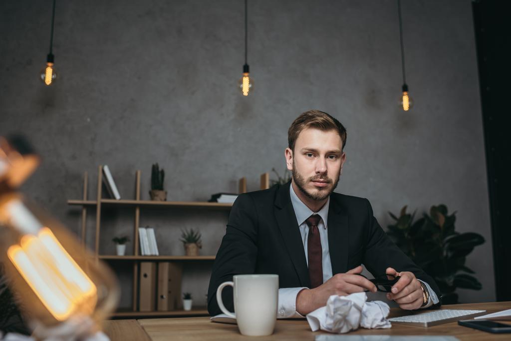 νεαρός επιχειρηματίας στο κοστούμι που κάθεται στο χώρο εργασίας - Φωτογραφία, εικόνα
