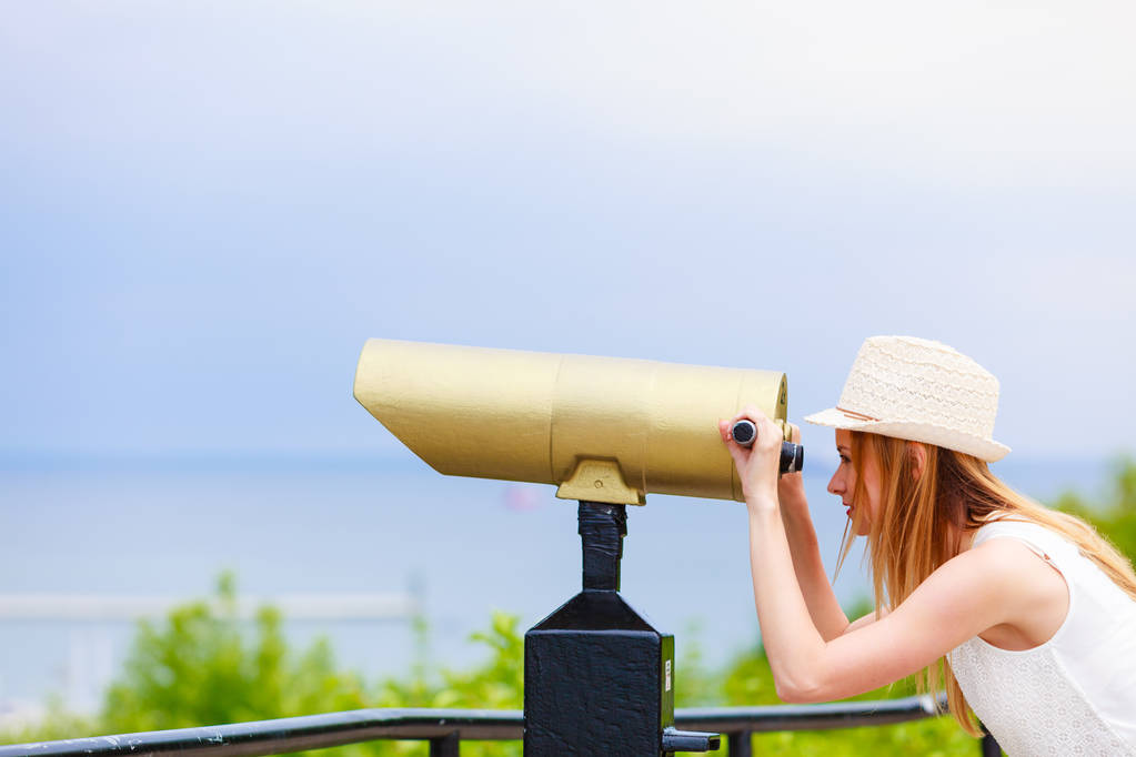 Жінка-турист з сонячним капелюхом дивиться через телескоп
 - Фото, зображення