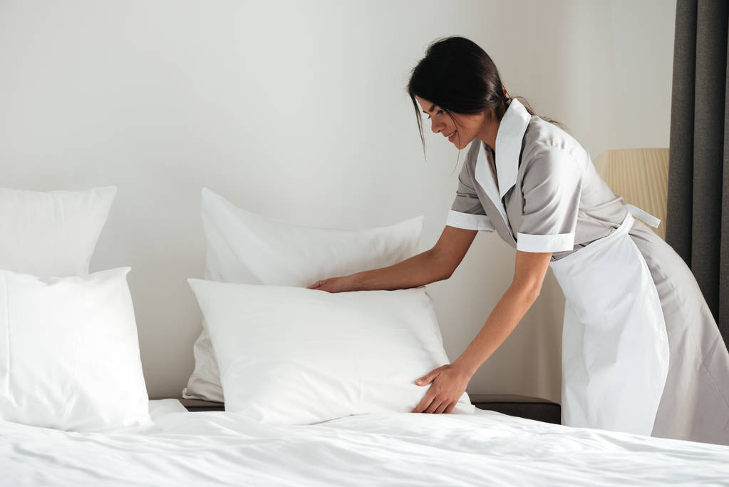 Jovem empregada doméstica do hotel configuração de travesseiro na cama
 - Foto, Imagem
