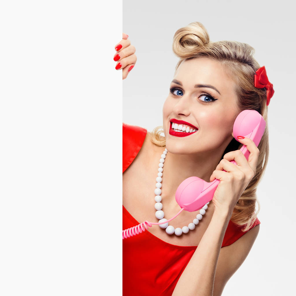 γυναίκα με τηλέφωνο, σε στυλ pin-up-φόρεμα, δείχνει κενός πινακίδα - Φωτογραφία, εικόνα