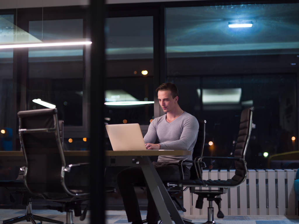 man aan het werk op laptop in donkere kantoor - Foto, afbeelding