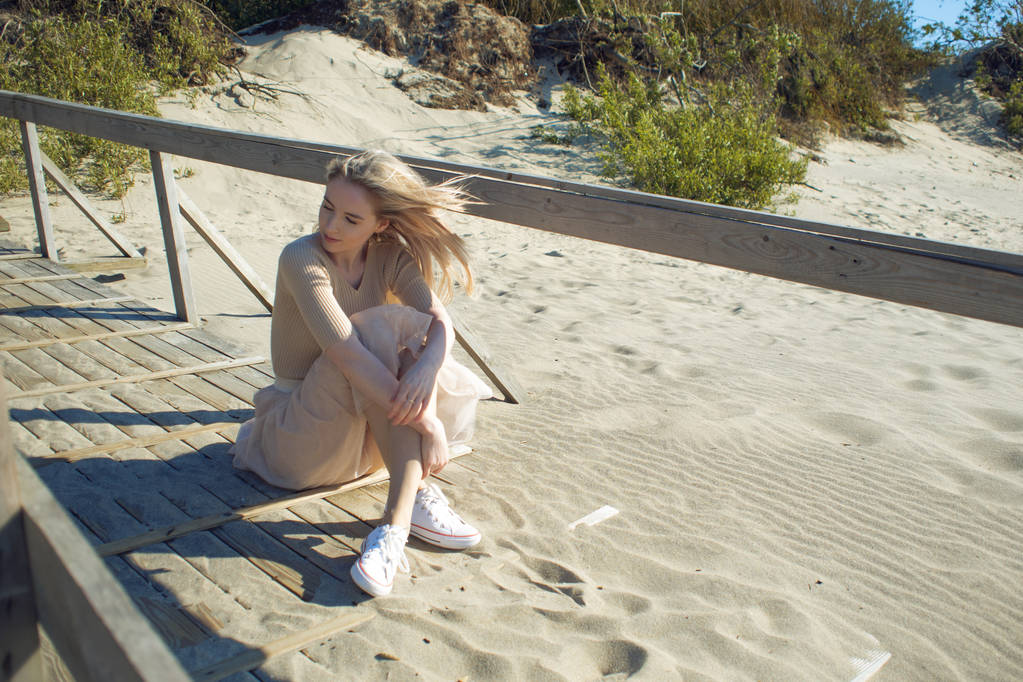 Veselá dívka na pláži. Mladá blond žena seděla na písku a těší hezké počasí - Fotografie, Obrázek