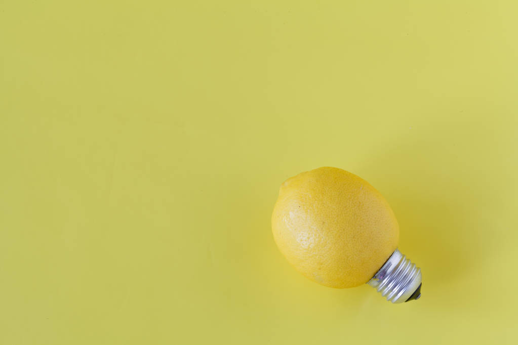 Δημιουργική ιδέα φωτογραφία ενός λεμονιού με μια λάμπα στο κίτρινο λεμονάτα - Φωτογραφία, εικόνα