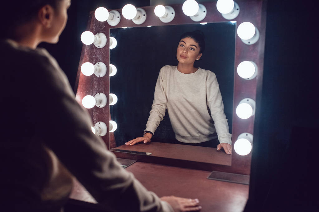 Aantrekkelijke brunette in een grijze trui kijkt in de spiegel. - Foto, afbeelding
