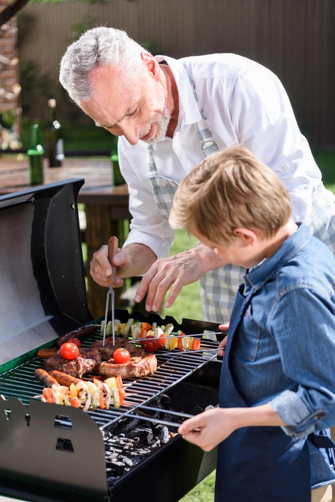 grand-père avec petit-fils préparant la viande sur le gril
 - Photo, image