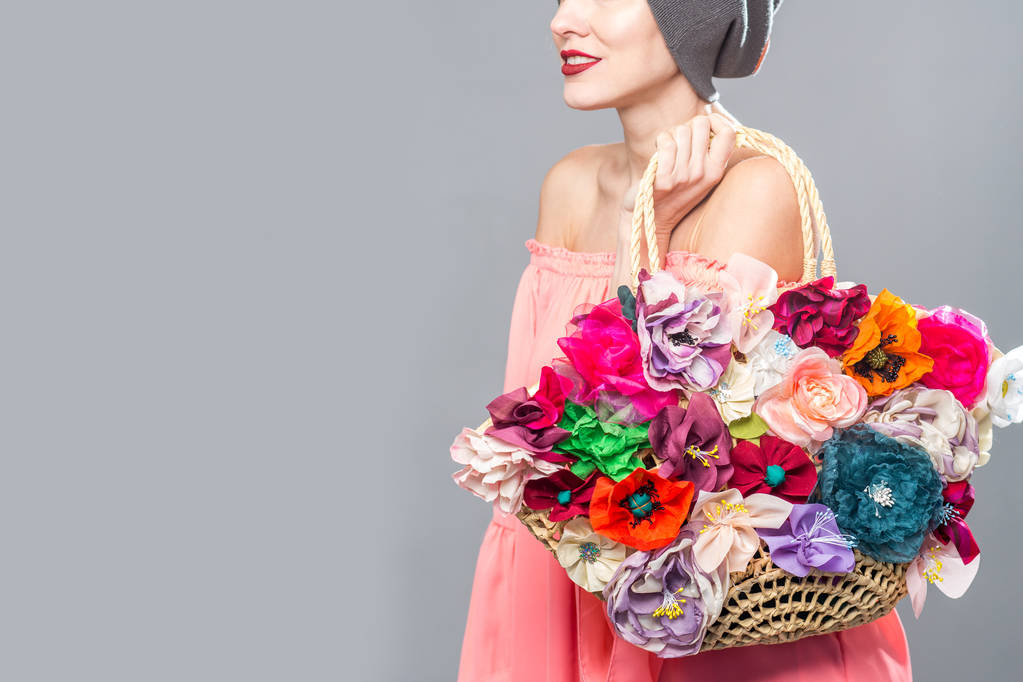 Mooie vrouw in roze jurk die bloemen tas geïsoleerd over grijs - Foto, afbeelding
