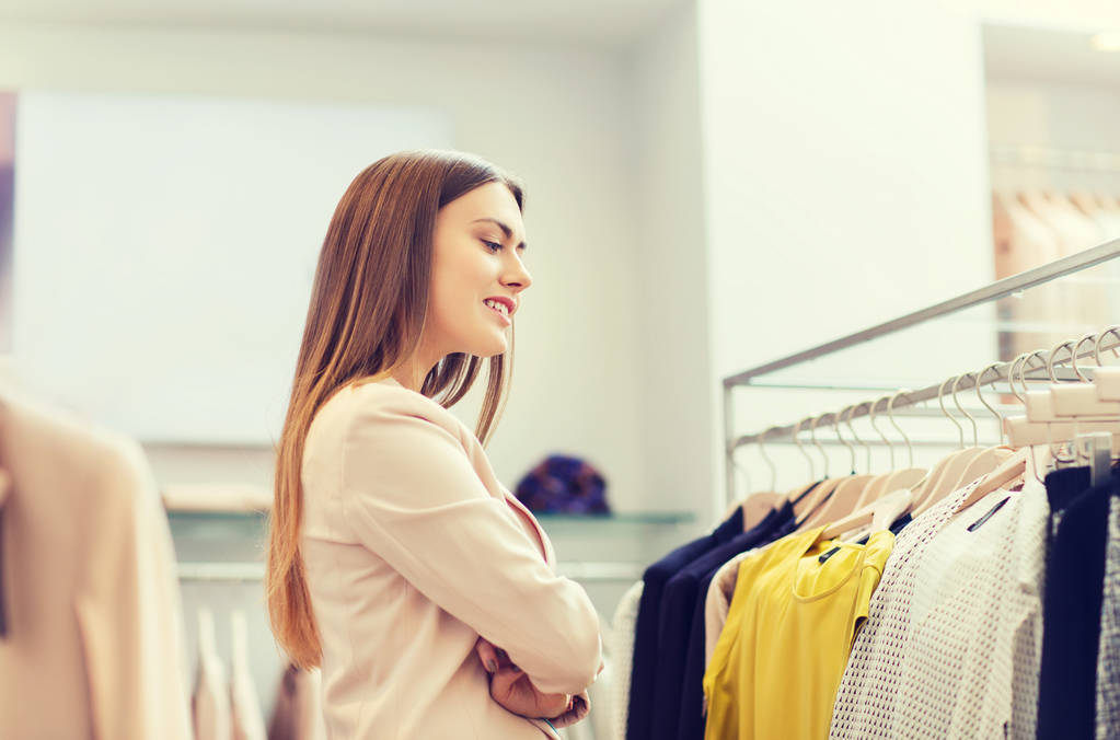 onnellinen nuori nainen valitsee vaatteita ostoskeskuksessa
 - Valokuva, kuva