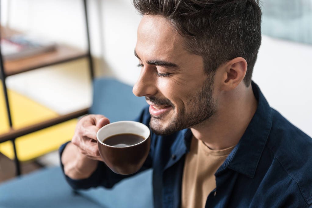 Cheerful handsome guy taking pleasure from hot drink - Photo, Image