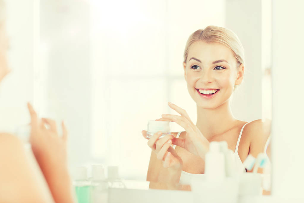 счастливая женщина наносит крем на лицо в ванной комнате
 - Фото, изображение