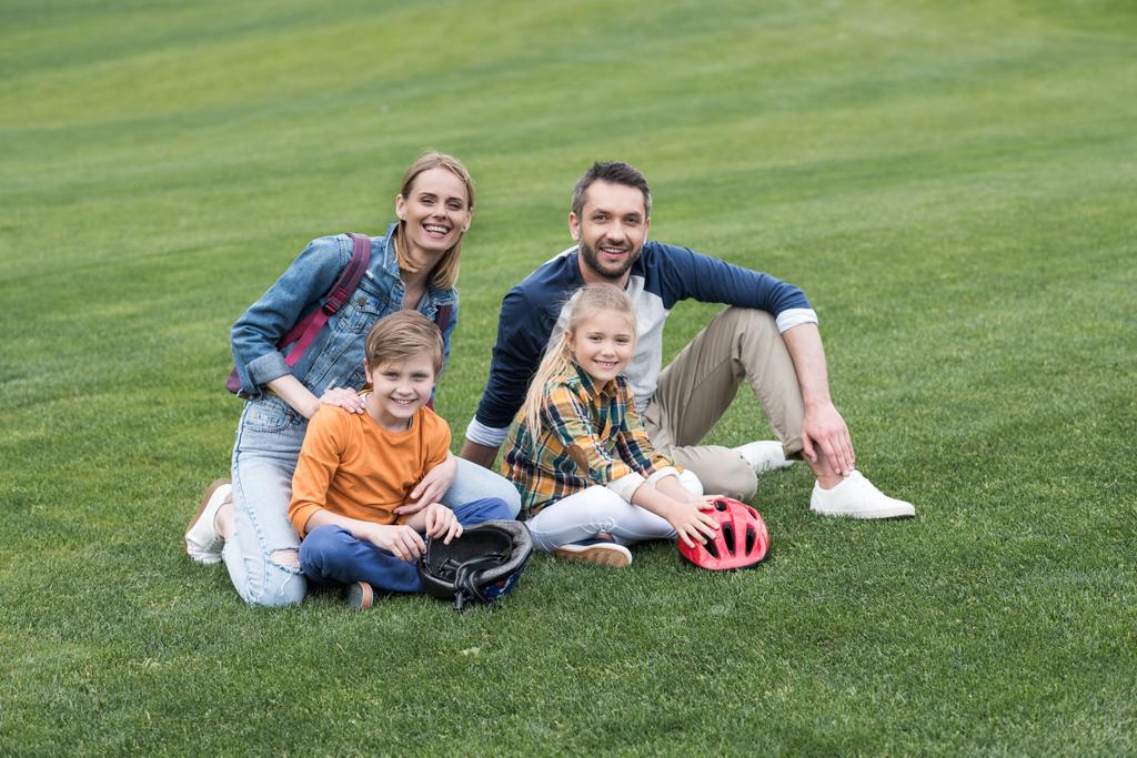улыбающаяся семья сидит на траве в парке
 - Фото, изображение