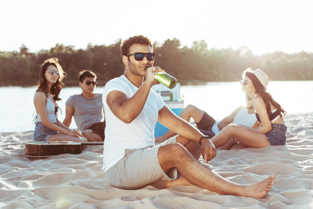 若い男がビーチでビールを飲む - 写真・画像