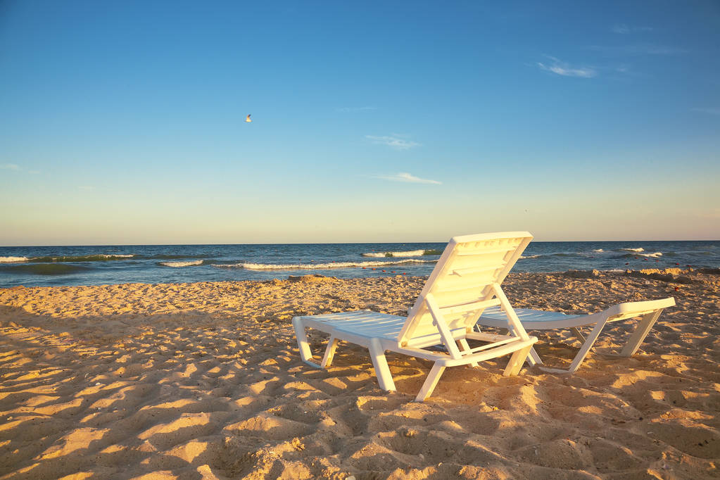 Kaksi kansituolia rannalla kirkas aurinko ja aallot
 - Valokuva, kuva