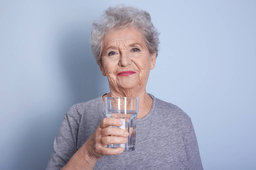 Літня жінка тримає склянку води
  - Фото, зображення