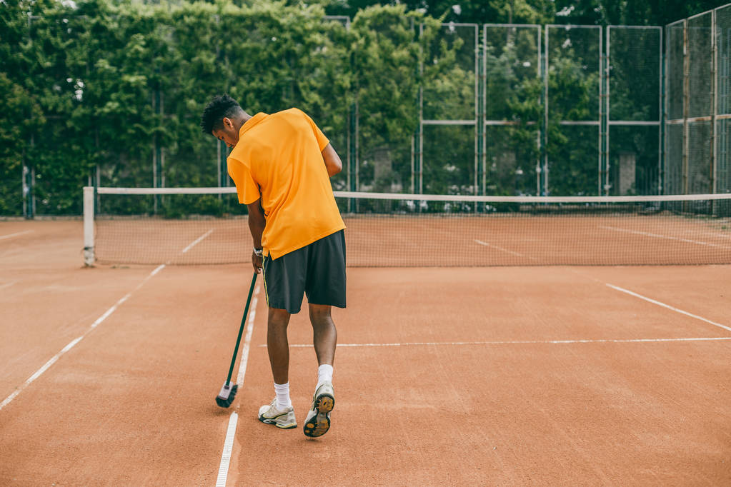 young man in a sports uniform is cleaning a tennis court - Photo, Image