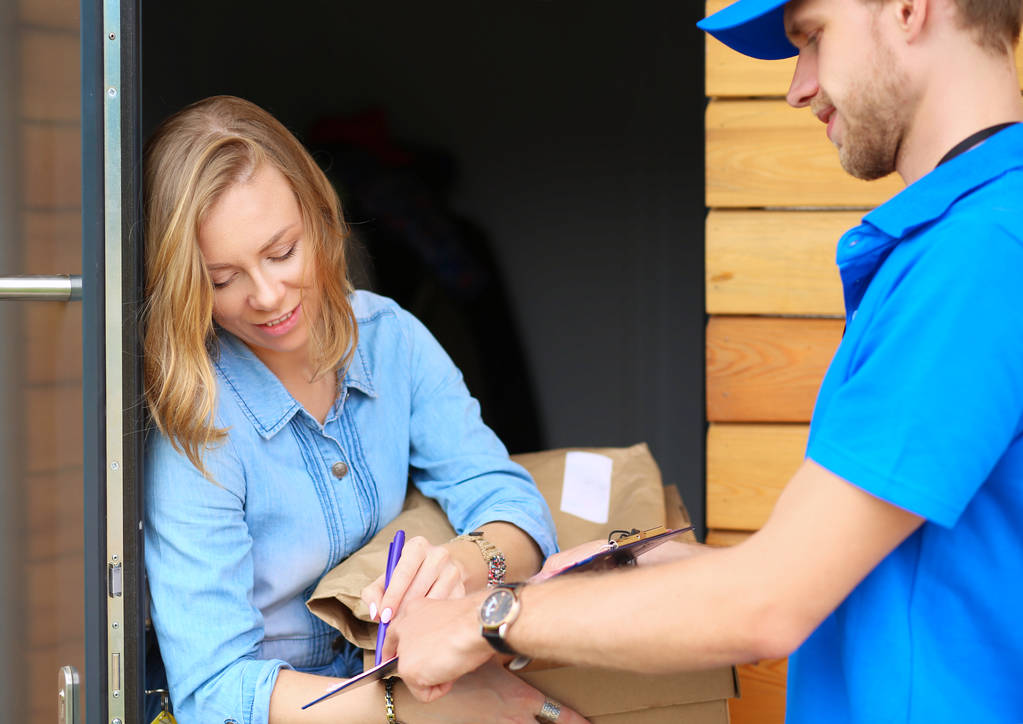 Usmívající se doručovatel v modré uniformě doručující balíček příjemci - koncept kurýrní služby - Fotografie, Obrázek