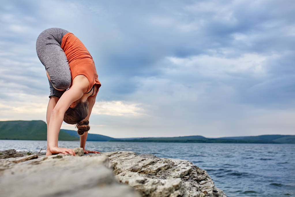 Attractive woman is practicing yoga on the stone near beautiful river. - Photo, Image