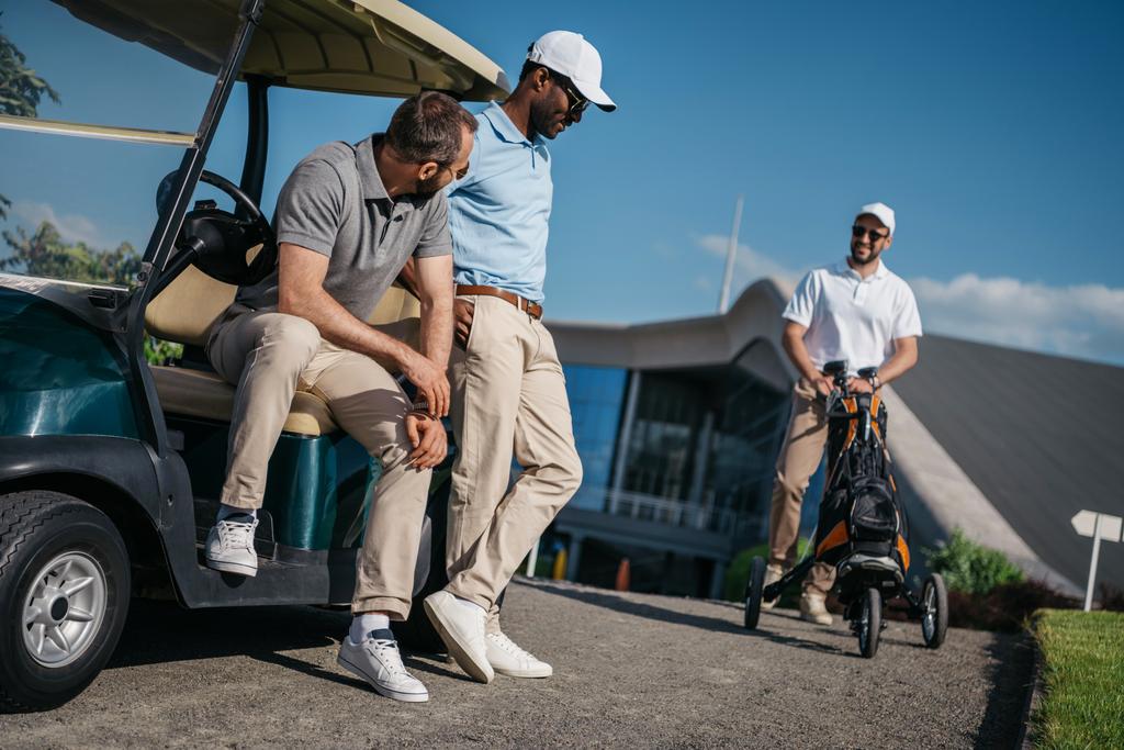 miehet seisomassa golfkärryn lähellä
 - Valokuva, kuva