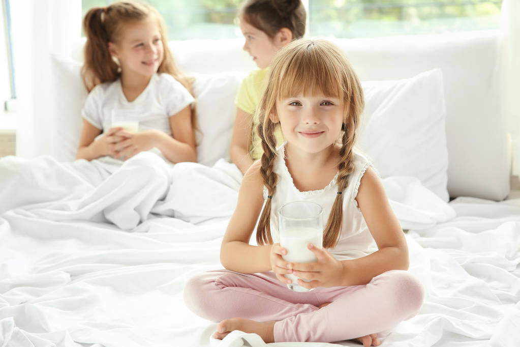 Küçük kız yatakta bardak süt ile oturan - Fotoğraf, Görsel