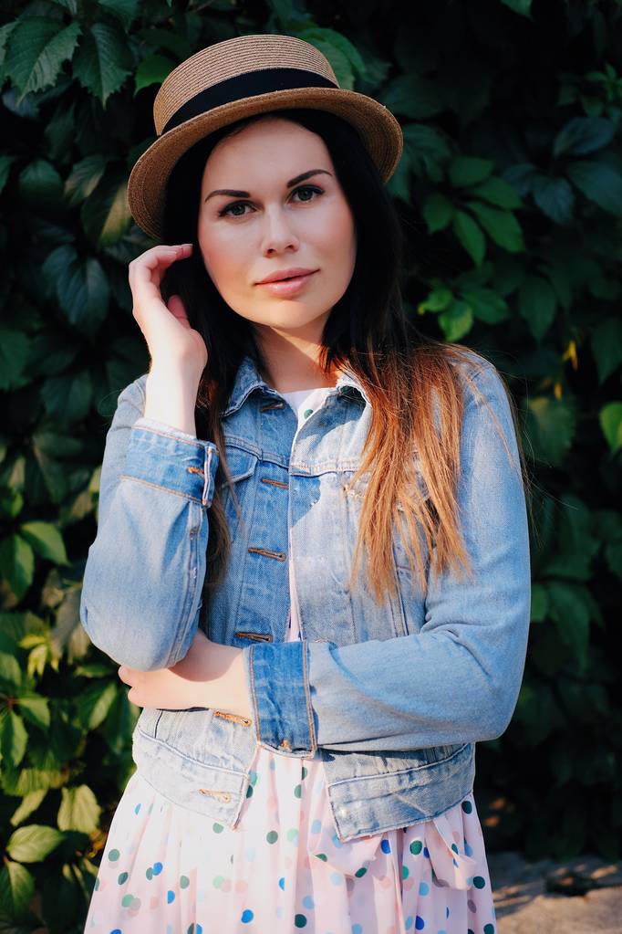 Outdoor summer smiling lifestyle portrait of pretty young woman In a denim jacket, hat and dress, having fun in the city in Europe in evening - Photo, Image