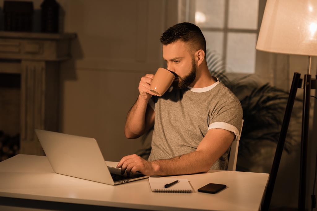 Mies juo kahvia työskennellessään Laptop
 - Valokuva, kuva