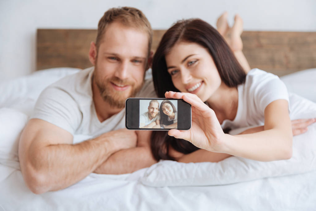 Porträt eines frisch verheirateten Paares beim Selfie im Bett - Foto, Bild