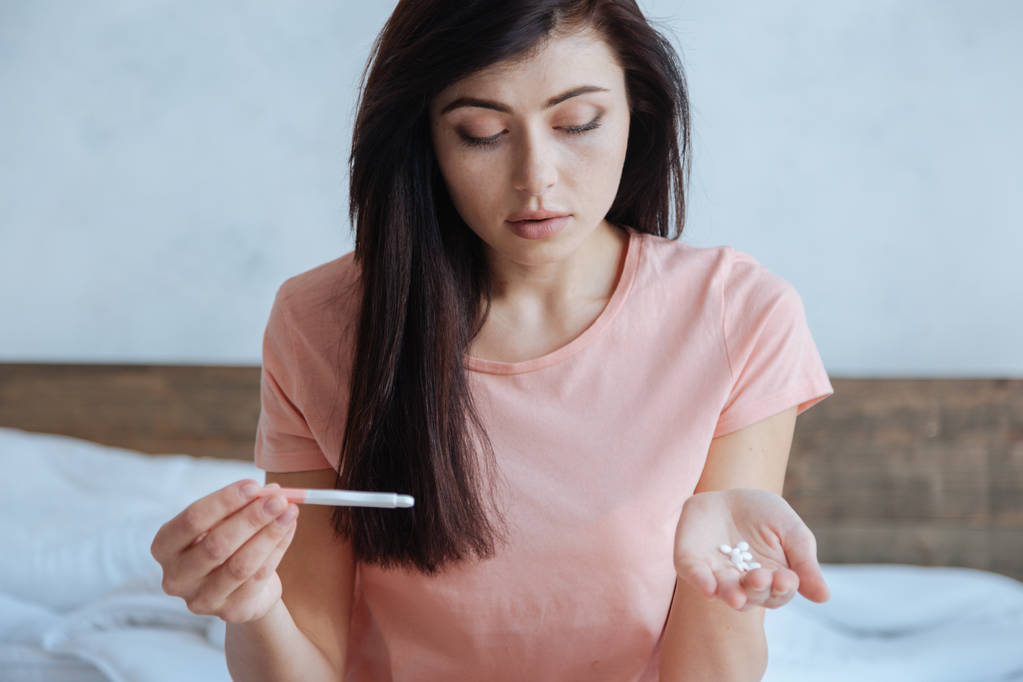 Portret van verwarde vrouw kijken pillen en zwangerschapstest - Foto, afbeelding