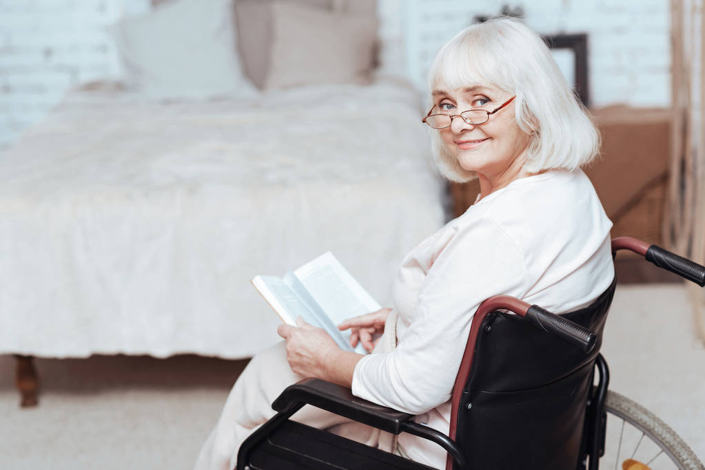 Θετική συνταξιούχος γυναίκα ανάγνωση βιβλίων στην αναπηρική καρέκλα στο σπίτι - Φωτογραφία, εικόνα