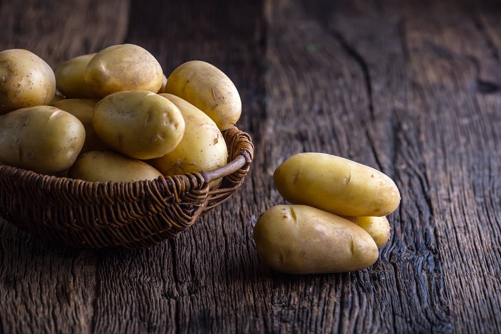 Verse rauwe aardappelen in mand op rustieke eiken bord - Foto, afbeelding