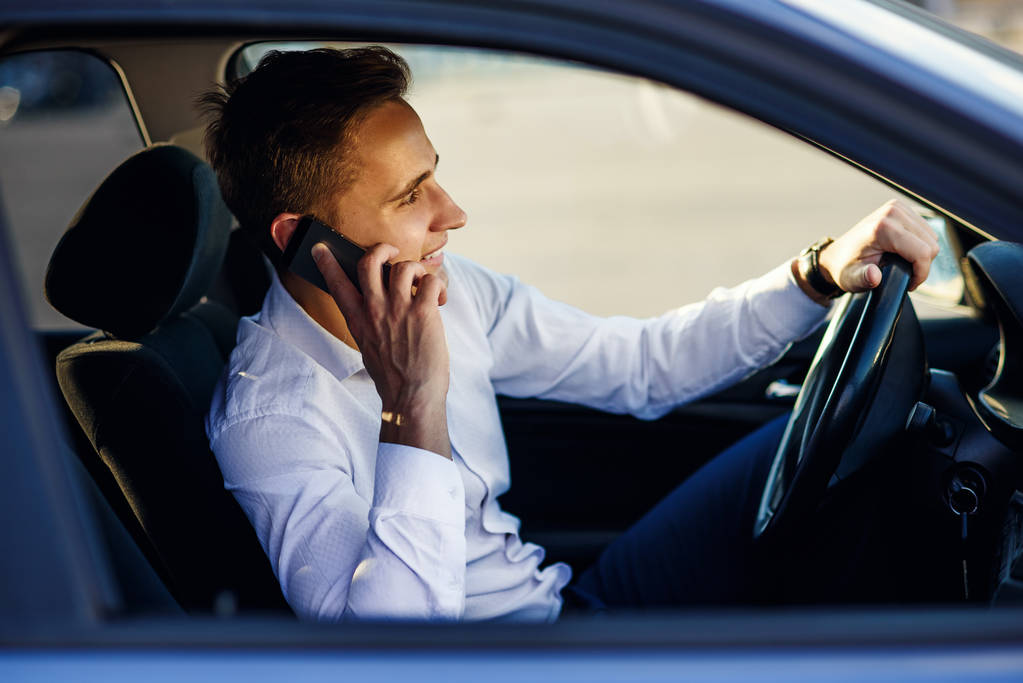 Beau homme d'affaires attrayant parlant avec le téléphone tout en conduisant une voiture dans la ville
 - Photo, image