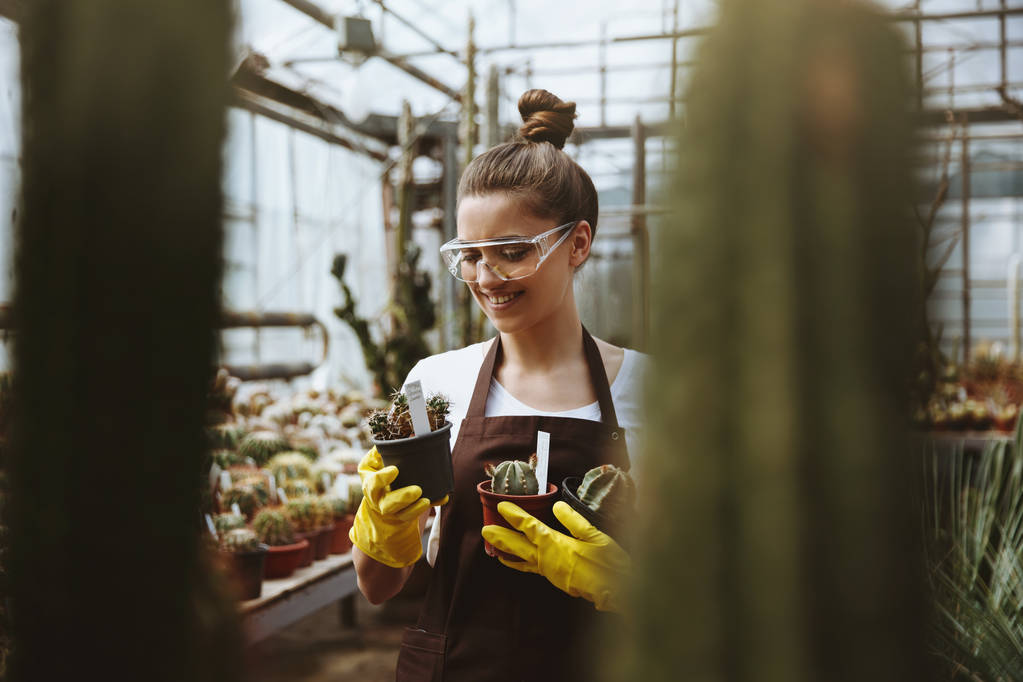 Joyeux jeune femme dans des lunettes debout dans la serre près des plantes
. - Photo, image